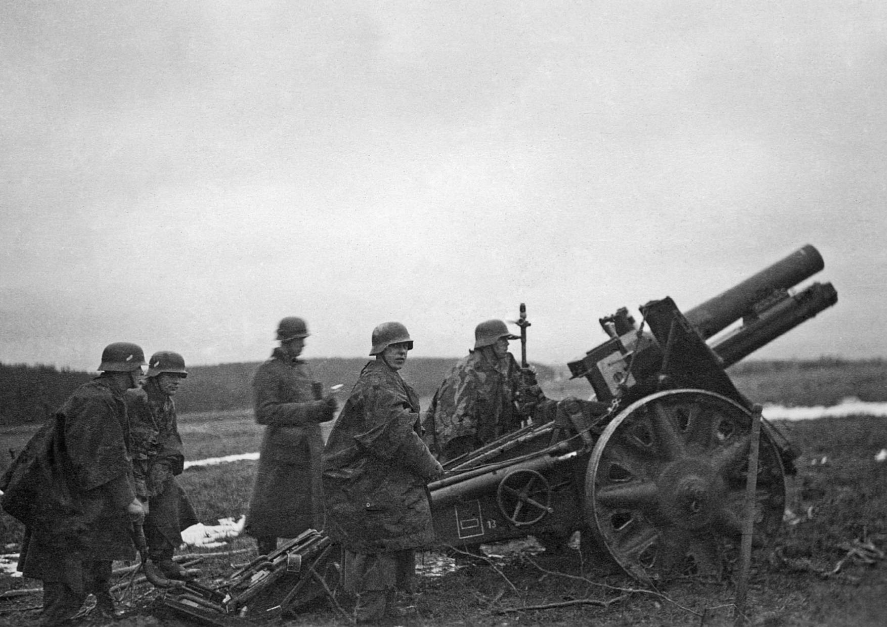 6 Απριλίου 1941. Γερμανός στρατιώτης προσαρμόζει τη θέση πυροβόλου των 15 εκ. με βάση τις συντεταγμένες που του διαβάζει ο επικεφαλής αξιωματικός, έχοντας ως στόχο ελληνική θέση της Γραμμής Μεταξά